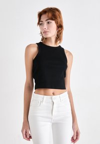 Top corto negro de tirantes con textura acanalada, escote redondo y diseño sin mangas, combinado con jeans blancos de cintura alta.