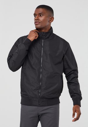 Giubbotto bomber nero con colletto alto, chiusura con zip, polsini e orlo a coste, e una texture liscia e leggermente lucida.