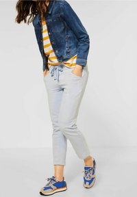 Jeansjacka, randig gul och vit tröja, ljusgrå sweatpants med dragsko, och blå sneakers med grå accenter.