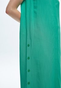 Abito in tessuto verde caratterizzato da una leggera texture, design dritto e sei bottoni coordinati lungo il lato sinistro per la chiusura.