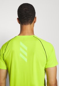 Neongrön träningströja med nätstruktur, svarta sömmar och tre reflekterande ränder på baksidan, korta ärmar och rund halsringning.
