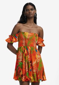 Olkapäältä avautuva mekko kirkkaan oranssista kankaasta, jossa on trooppisia lehtikuvioita ja kukkakuosia, smokk bodice ja röyhelöhihoilla.