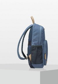 Blauwe stoffen rugzak met een textuur, voorzien van een gaas zijzak en een bruine leren accent aan de onderkant. Zijaanzicht.