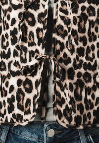 En leopardmönstrad vadderad jacka knuten i midjan över en grå skjorta instoppad i blå denimjeans.
