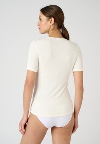 Short-sleeve, light cream top made of soft fabric, featuring a simple round neckline and fitted silhouette, shown from the back.