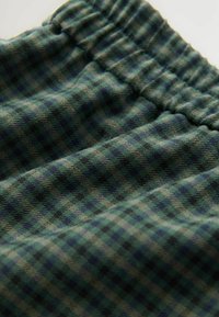 Grüner und blauer karierter Stoff mit einer weichen Textur, der einen gerafften Bund hat und ein Muster aus kleinen Quadraten in unterschiedlichen Farbtönen zeigt.