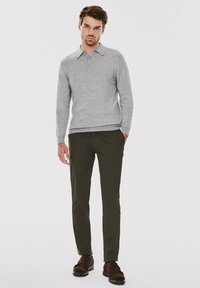 Szara koszulka polo z długimi rękawami, z kołnierzykiem i trzema guzikami, zestawiona z ciemnozielonymi spodniami slim fit i brązowymi butami. Gładka faktura.
