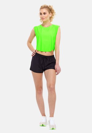 Neon grön kort topp och svarta shorts med dragsko i midjan. Modellen bär vita skor med gröna accenter. Enkel vit bakgrund.