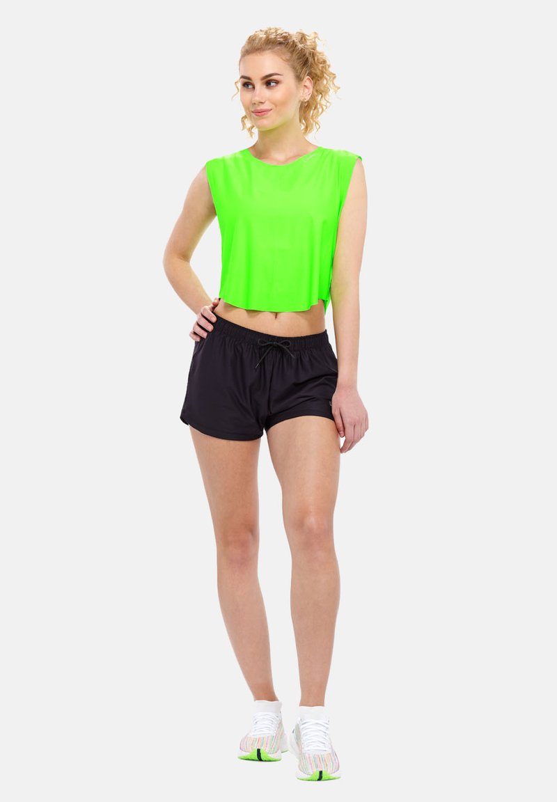 Neon zelena kratka majica i crne šortse s vezicom u struku. Model nosi bijele cipele s zelenim detaljima. Obična bijela pozadina.