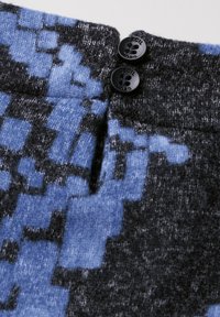 Strickstoff mit einem pixelierten Design in Blau und Schwarz. Zwei schwarze Knöpfe betonen den Taillenbund und fügen Textur und Detail hinzu.