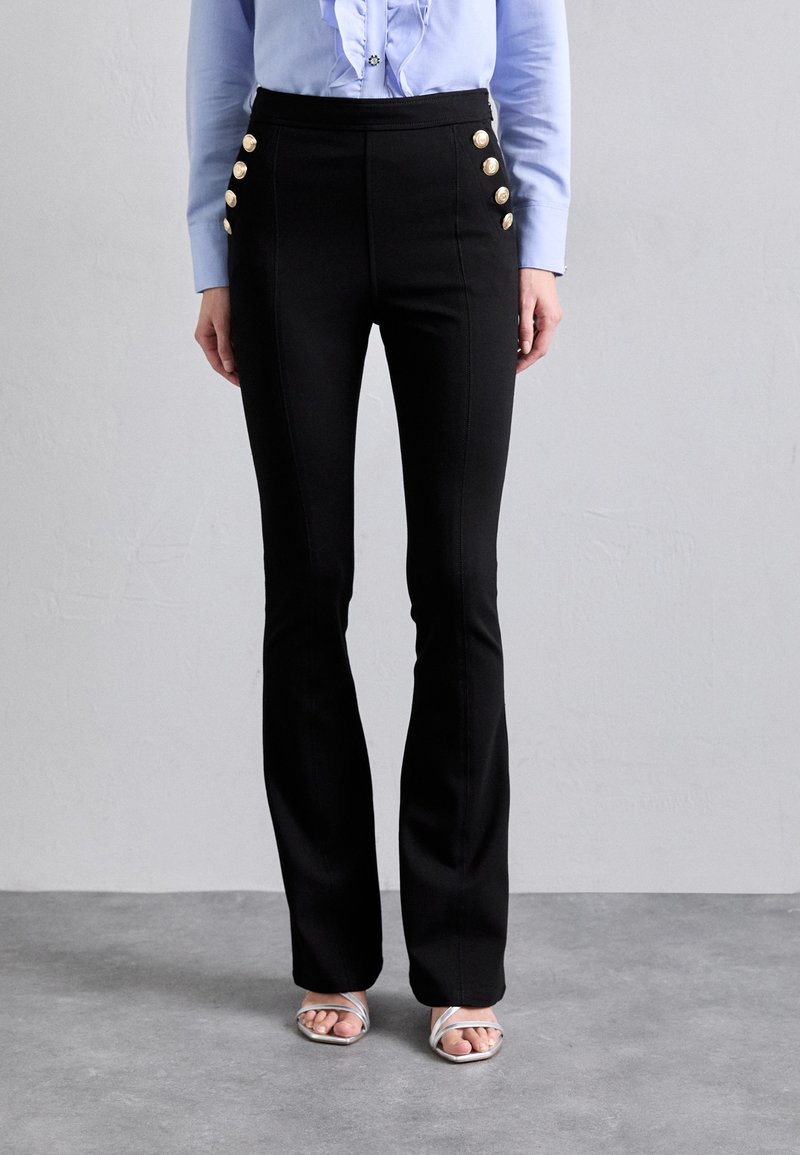 Black flared pants with gold button accents on the sides, high-waisted design, and smooth texture, paired with a light blue blouse.