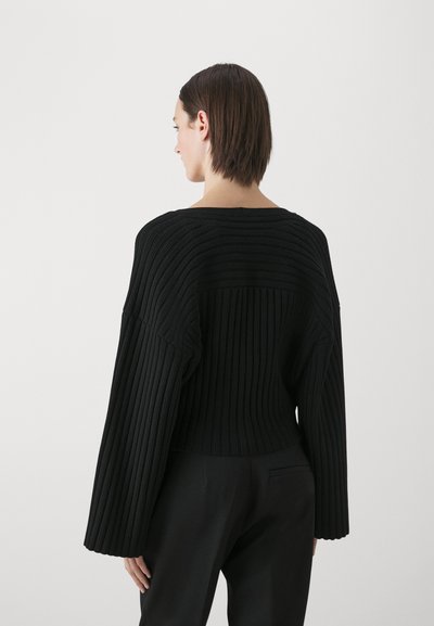 Sweater preto canelado com um design amplo e cropped, apresentando mangas longas e largas e um decote arredondado, destacando um material de malha texturizada.
