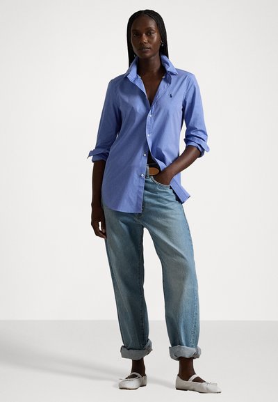 Chemise bleu clair à manches retroussées, assortie à un jean décontracté en denim bleu clair et des ballerines blanches. Présente un petit logo sur la poitrine.