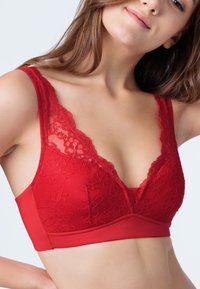 Bralette in pizzo rosso con scollatura a V profonda, dettagli in pizzo floreale lungo le spalline e una banda liscia sottostante. Tessuto morbido e materiale elastico.