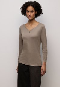 Top beige chiaro a maniche lunghe con scollo a V e dettaglio con due bottoni. Tessuto morbido con una trama liscia, abbinato a pantaloni scuri dalla texture lavorata.