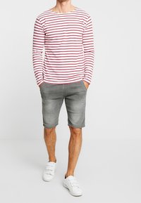 Camisa de manga larga a rayas rojas y blancas combinada con pantalones cortos de mezclilla grises, complementada con zapatillas blancas. Textil casual y corte relajado.