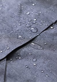 Voděodolná tmavě šedá tkanina s viditelnými kapkami vody, která ukazuje strukturu a hladký povrch, s viditelnými záhyby v materiálu.
