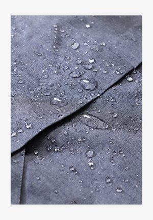 Wodoodporny ciemnoszary materiał z widocznymi kroplami wody, ukazujący teksturę i gładkie wykończenie, z widocznymi fałdami w materiale.