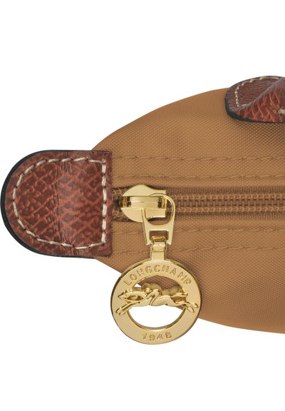Beige Stoffbeutel mit einer strukturierten braunen Lederakzent. Verfügt über einen goldenen Reißverschluss und ein rundes goldfarbenes Metalletikett mit der Gravur "LONGCHAMP 1948".