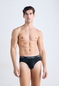 Schwarze Baumwollunterhosen mit einem weißen Calvin Klein-Logo am Bund. Sie haben eine glatte Textur und ein enganliegendes Design, das die Körperform betont.