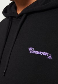Czarna bawełniana bluza z kapturem z purpurowym logo kwiatowym na lewej części klatki piersiowej. Miękka tekstura, z kapturem ze sznurkiem i ściągaczami przy mankietach.