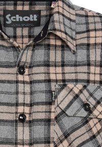 Camisa de franela a cuadros en tonos gris y negro con acentos beige, que presenta un cierre con botones, cuello y un pequeño bolsillo en el pecho. Hecha de material suave.