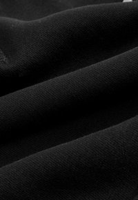 Tissu en coton noir avec une texture douce, présentant plusieurs couches et des variations subtiles de nuances et de surface.