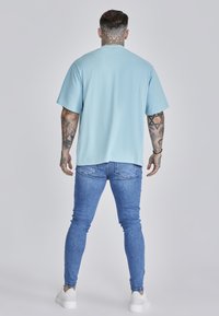 Világoskék, rövid ujjú póló, laza fazon, kék skinny farmernadrággal és fehér sportcipővel párosítva. Simító anyag, egyszínű dizájn, minták nélkül.