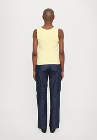 Gelbes geripptes Tanktop mit gewelltem Saum, kombiniert mit dunkelblauen Cargo-Jeans mit Seitentaschen und geradem Bein.