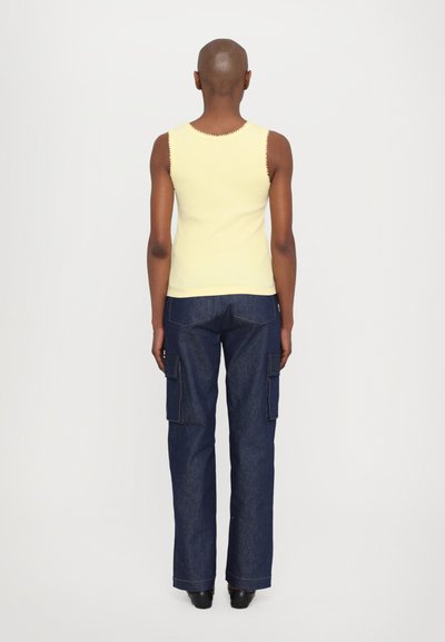 Gelbes geripptes Tanktop mit gewelltem Saum, kombiniert mit dunkelblauen Cargo-Jeans mit Seitentaschen und geradem Bein.