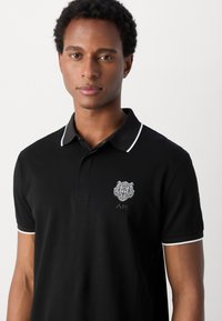 Zwarte polo met witte accenten, met een leeuw-embleem en logo op de borst. Gemaakt van katoen met een klassieke pasvorm en kraag.