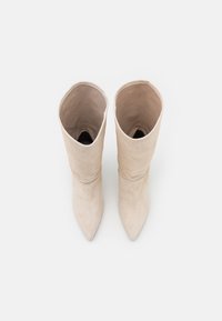 Botas de ante beige de altura hasta la rodilla con punta estrecha y un diseño de puño doblado. Textura suave, estilo minimalista. Sin herrajes ni patrones visibles.