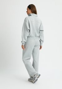 Sudadera gris claro y pantalones de chándal a juego, corte relajado, textura suave, con un cuello alto y puños elásticos. Zapatillas grises con detalles.