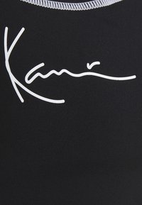 Svart tygskjorta med en vit signaturdesign. Texturen är jämn, med kontrasterande sömmar runt halsringningen.