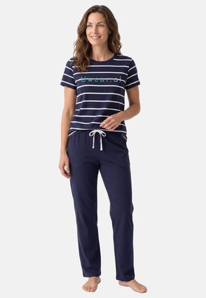 Donna in piedi a piedi nudi che indossa una maglietta a maniche corte a righe blu navy e bianco con testo "Uwear.ai" e pantaloni blu navy con coulisse.
