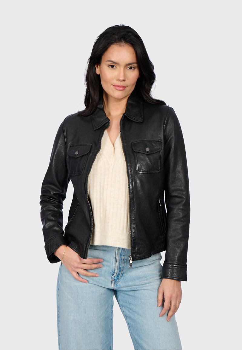Black leather jacket with a zip front, collar, and two chest pockets. Worn over a light cream sweater and paired with light blue jeans.