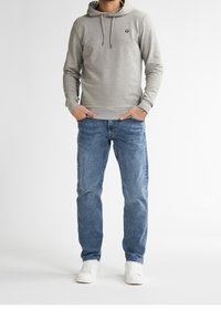 Felpa grigia con cappuccio e lacci, indossata con jeans in denim azzurri e sneakers bianche, presenta un logo sul petto e polsini a coste.