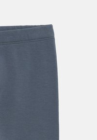 Gray cotton leggings with a smooth texture and elastic waistband. Close-up view shows stitching detail along the top edge.