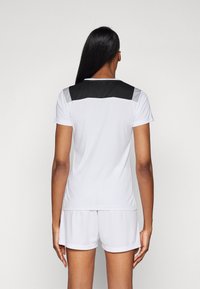Hvitt idrettsg shirt med en svart og grå skulderpanel, parret med matchende hvite shorts. Laget av et glat, fukttransporterende materiale.