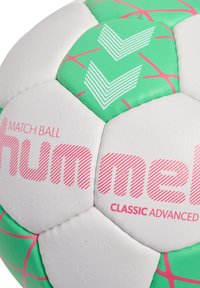 Pallone da calcio bianco e verde con accenti rosa, superficie testurizzata e motivi a zigzag. Nome del marchio "Hummel" in evidenza.