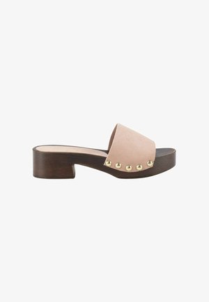 Sandalia de pala abierta con tacón bajo de madera y una amplia tira de ante beige con cinco tachuelas doradas en el lateral exterior.