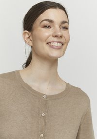 Beige knitted cardigan with a round neckline, featuring evenly spaced buttons at the front and a soft, smooth texture.