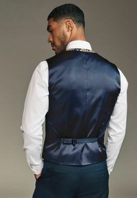 Marineblaues Satin-Weste mit einem eleganten Design, das über einen Schnallenverschluss und florale Akzente am Kragen verfügt, getragen über einem weißen Hemd.