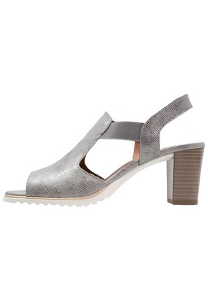 Srebrne sandały z odkrytymi palcami na szpilce typu slingback, z fakturowaną cholewką, elastycznymi bocznymi paskami, białą podeszwą i masywnym, drewnianym obcasem o średniej wysokości.