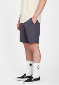 Gray shorts made of fabric with a smooth texture, featuring side pockets, paired with black slip-on shoes and white logo socks.
