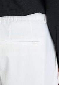 White trousers with a smooth texture, featuring a back pocket and subtle "BOSS" logo. Paired with a textured black top.