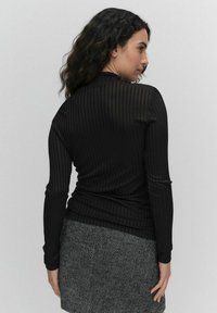 Mustan ribbitekstiilin pitkähihaisessa paidassa on korkea kaulus ja se on tiukka malli. Yhdistettynä teksturoituun musta-valkoiseen houndstooth-hameeseen.