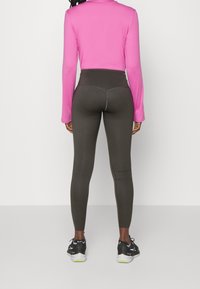 Top de manga larga ajustado en color rosa y leggings de talle alto en verde oliva con un acento de costura, combinados con zapatillas deportivas negras.