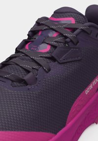 Κοντινή λήψη σκούρου μοβ και ροζ αθλητικού παπουτσιού Gore-Tex με υφασμάτινη υφή, κορδόνια και ενισχυμένες οπές.