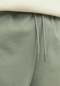 Pantalons de jogging vert clair avec une texture douce, dotés d'une taille à cordon de serrage et d'extrémités en textile assorties. Design simple, détails minimaux.